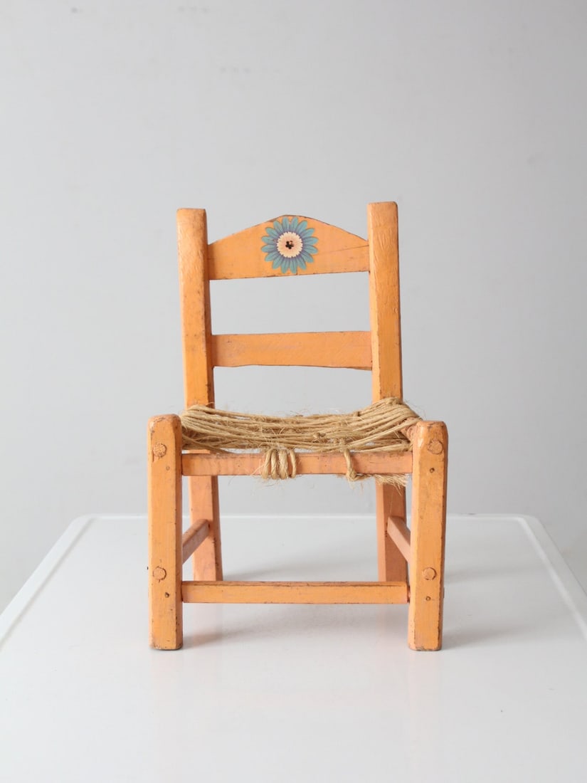 Vintage Mexican Child's Chair with Floral Stencil Detail: Vintage Mexican Child's Chair with Floral Stencil Detail This charming vintage Mexican child's chair showcases a warm peach finish complemented by a delicate floral stencil at the back. Its woven fibe