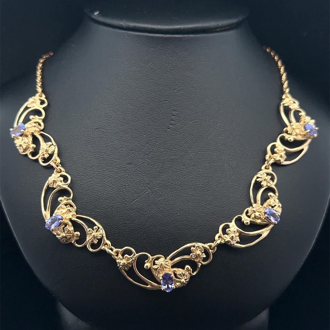 Floral Openwork Necklace with 2ctw Oval Tanzanite in Yellow Gold: Floral Openwork Necklace with 2ctw Oval Tanzanite in Yellow Gold This vintage floral necklace features five natural oval brilliant cut tanzanite gemstones in a striking violetish blue color, with a to