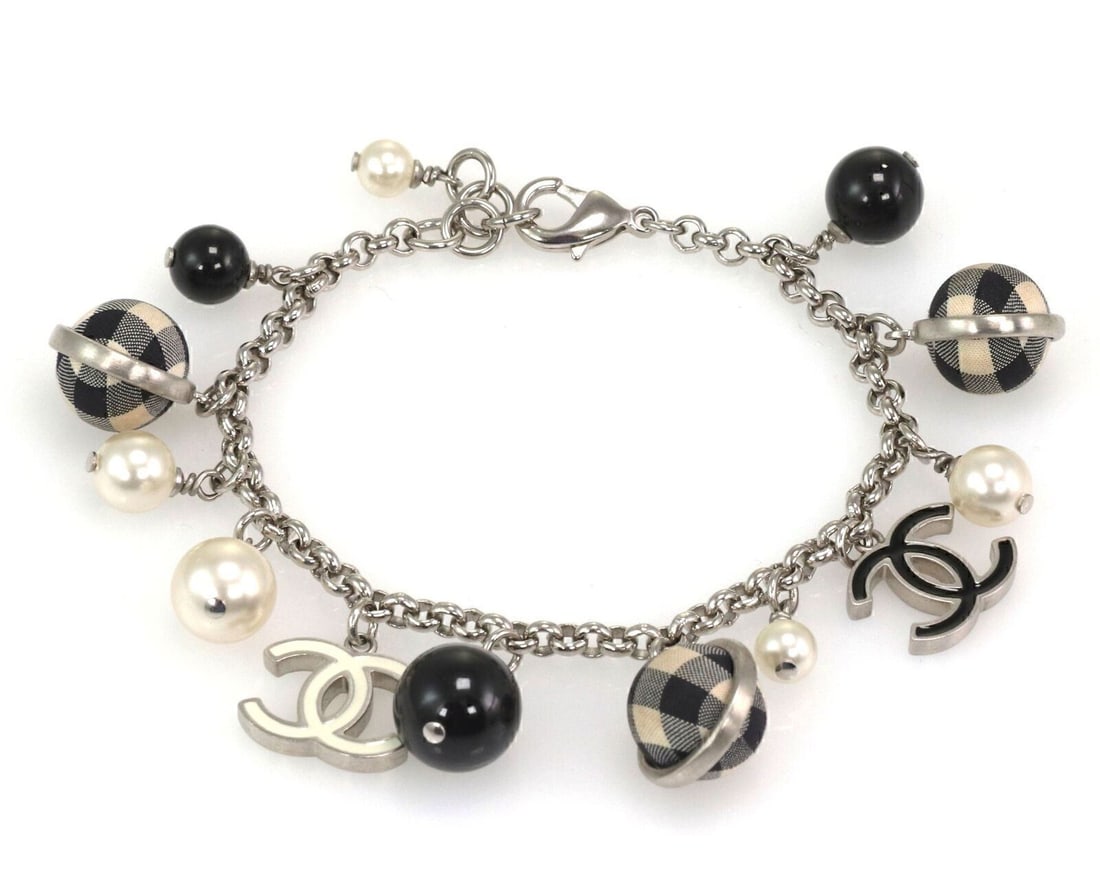 Chanel charm bracelet with C logo and faux pearls: Chanel charm bracelet with C logo and faux pearls This authentic Chanel charm bracelet features silver tone metal, black and white checkered beads, faux pearl accents, and signature C logo charms. The