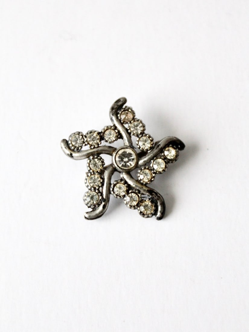 Mid Century Silver Tone Swirling Star Brooch with Rhinestones: Mid Century Silver Tone Swirling Star Brooch with Rhinestones This vintage rhinestone star brooch from the 1950s-1960s features a swirling celestial star design adorned with sparkling rhinestones set 