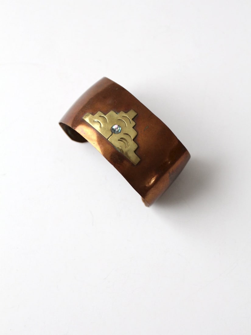 1960s Vintage Mexican Copper Cuff with Brass Pyramid and Abalone Inlay: 1960s Vintage Mexican Copper Cuff with Brass Pyramid and Abalone Inlay Discover a stunning piece of artistry with this vintage Mexican copper cuff from the 1960s. This wide cuff showcases a striking b