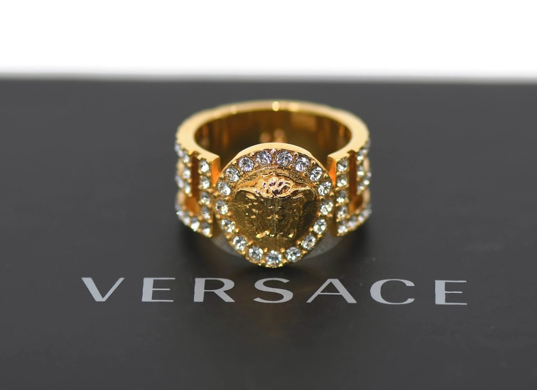 Size 8.5 gold plated Versace ring with 15mm width: Size 8.5 gold plated Versace ring with 15mm width This pre-owned Versace ring features a gold plated finish and is designed in size 8.5. The ring has a width of 15mm and weighs 8.2 grams, offering a b