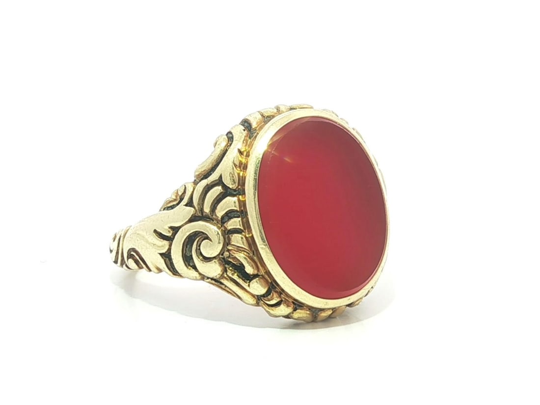 Carnelian Scrollwork Band in 14k Yellow Gold with Oval Bezel Setting: Carnelian Scrollwork Band in 14k Yellow Gold with Oval Bezel Setting This antique ring features an oval-cut, natural carnelian gemstone in a bezel setting, highlighted by intricate repousse scrollwork
