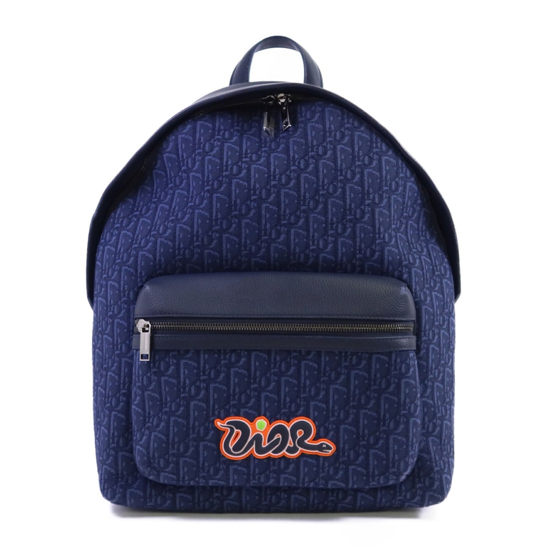 Dior x Kaws Rider 2.0 Navy Oblique Canvas and Leather Rucksack Backpack: Dior x Kaws Rider 2.0 Navy Oblique Canvas and Leather Rucksack Backpack This Christian Dior Rider 2.0 zipped backpack is crafted from navy Oblique canvas with leather accents. It features a rucksack b