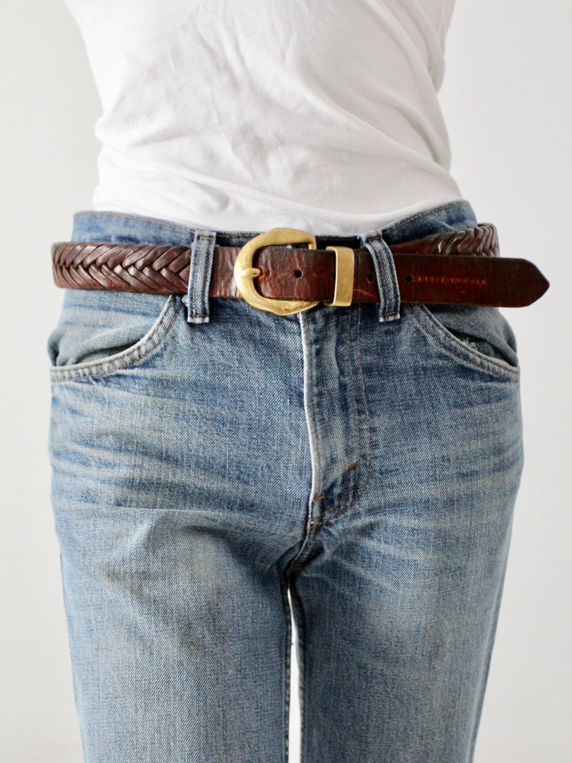 1970s Vintage Braided Leather Belt with Brass Buckle: 1970s Vintage Braided Leather Belt with Brass Buckle This vintage 1970s braided leather belt features a rich brown leather body adorned with a dynamic fishtail braid pattern. The belt is secured with 