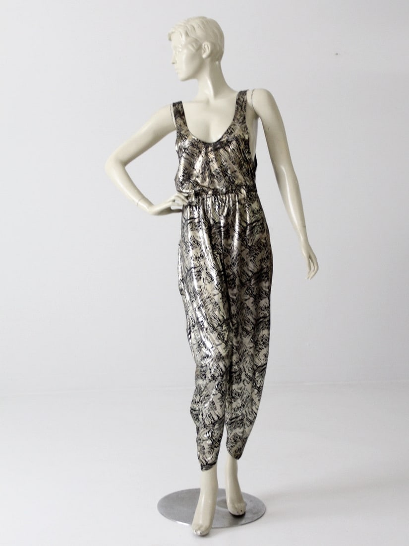 1980s Metallic Disco Jumpsuit Black Silver Gold Harem Style: 1980s Metallic Disco Jumpsuit Black Silver Gold Harem Style Step back into the vibrant 1980s with this stunning metallic disco jumpsuit. This eye-catching piece features a sleek black and silver-gold 