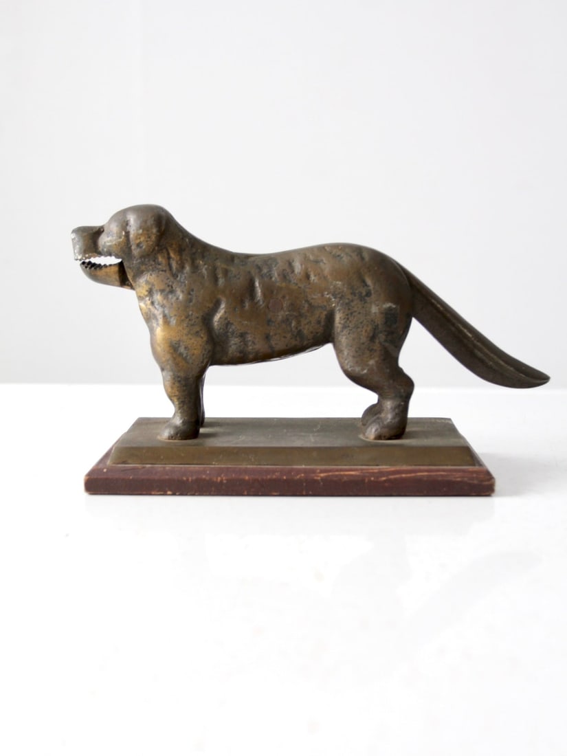 Solid Brass Dog Form Nutcracker on Wooden Base Antique Accent: Solid Brass Dog Form Nutcracker on Wooden Base Antique Accent This antique dog-shaped nutcracker is crafted from solid brass and features a naturally aged patina. Set on a wood base, it showcases earl