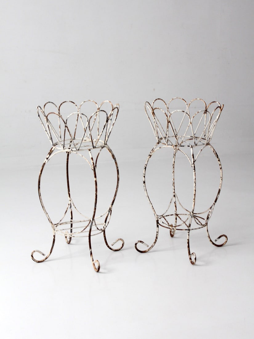 Pair of Vintage White Wirework Plant Stands: Pair of Vintage White Wirework Plant Stands This pair of vintage metal plant stands features an open wirework design with looping curves and scalloped rims. Each stand has a white painted finish with 