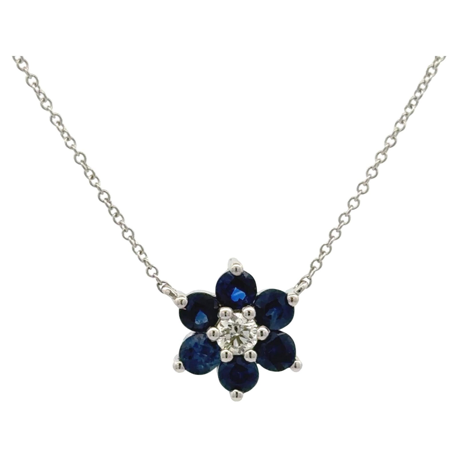 14k White Gold Floral Sapphire Diamond Pendant Necklace: 14k White Gold Floral Sapphire Diamond Pendant Necklace This elegant necklace is crafted from 14 karat white gold and features a flower-shaped cluster pendant. At the center of the pendant is a round 