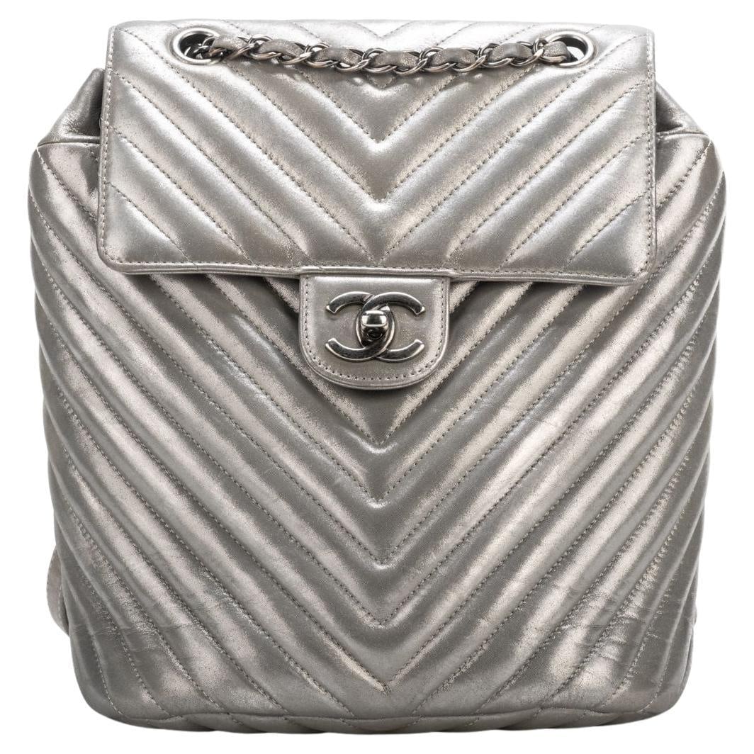 Chanel Silver Lambskin Chevron Backpack Collection 22 with Authenticity: Chanel Silver Lambskin Chevron Backpack Collection 22 with Authenticity This exquisite Chanel backpack is crafted from luxurious silver lambskin featuring a stylish chevron design. It boasts a height 