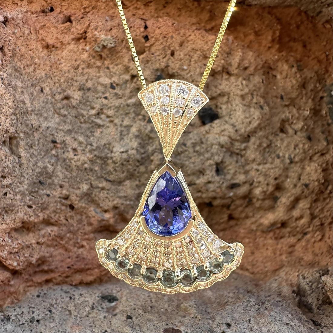 14k Yellow Gold Fan Pendant with Tanzanite Alexandrite Diamonds: 14k Yellow Gold Fan Pendant with Tanzanite Alexandrite Diamonds This elegant pendant features a flared fan design crafted in solid 14k yellow gold. The centerpiece is a pear-cut natural tanzanite with