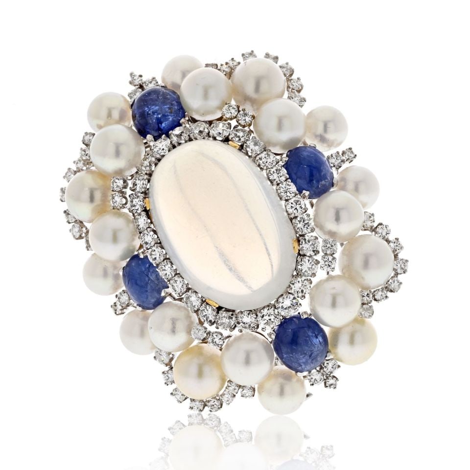 David Webb 1960s Platinum Moonstone Sapphire Diamond Brooch: David Webb 1960s Platinum Moonstone Sapphire Diamond Brooch This exquisite David Webb brooch, dating back to the 1960s, showcases a stunning elongated cabochon moonstone at its center, beautifully sur