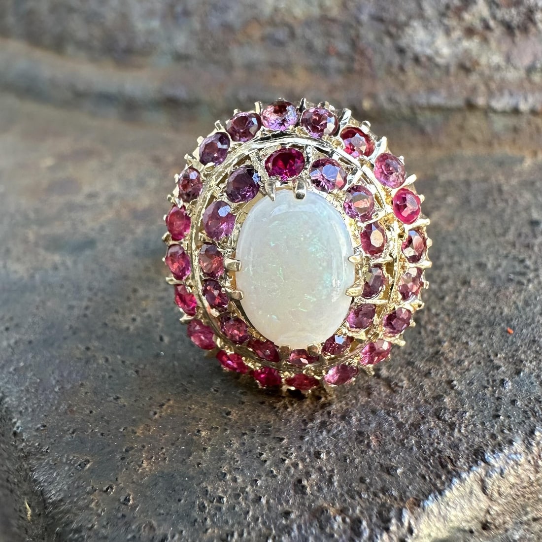 14k Yellow Gold Vintage Ring with Cabochon Opal and Pink Stone Double Halo: 14k Yellow Gold Vintage Ring with Cabochon Opal and Pink Stone Double Halo This vintage retro ring features a natural cabochon-cut opal set in solid 14k yellow gold. The opal displays a white base wit