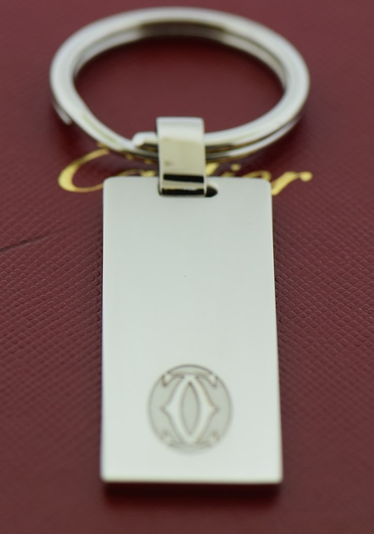 Cartier silver stainless steel 50mm key ring with box: Cartier silver stainless steel 50mm key ring with box This Cartier key ring is crafted from stainless steel and features a sleek silver finish. Designed for unisex use, it offers a modern and sophisti