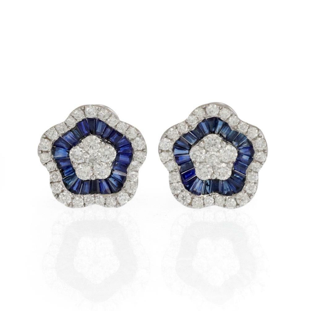 18k White Gold Diamond Sapphire Flower Huggie Earrings: 18k White Gold Diamond Sapphire Flower Huggie Earrings This pair of huggie earrings is crafted from 18k white gold and features a large, concave flower design with wave-shaped petals measuring approxi