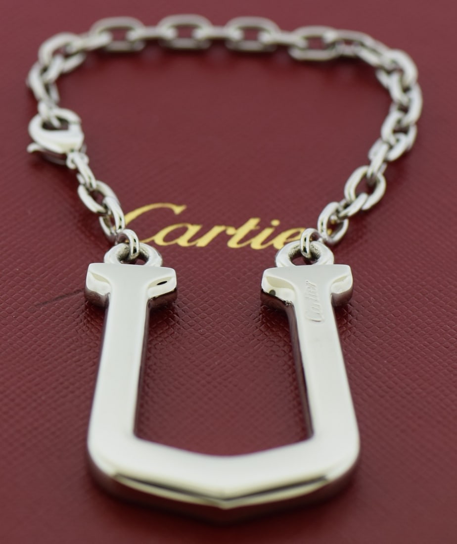 Cartier stainless steel U key ring with box 43mm: Cartier stainless steel U key ring with box 43mm This pre-owned Cartier key ring is crafted from durable stainless steel and features a sleek silver finish. Designed for unisex use, it offers both sty