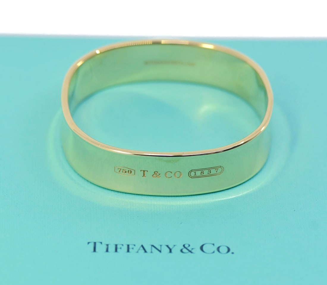Tiffany & Co 18K Yellow Gold Hinged Bangle Bracelet 15mm: Tiffany & Co 18K Yellow Gold Hinged Bangle Bracelet 15mm This exquisite bracelet from Tiffany & Co. showcases a timeless bangle style crafted from 18K yellow gold, radiating elegance and sophisticatio