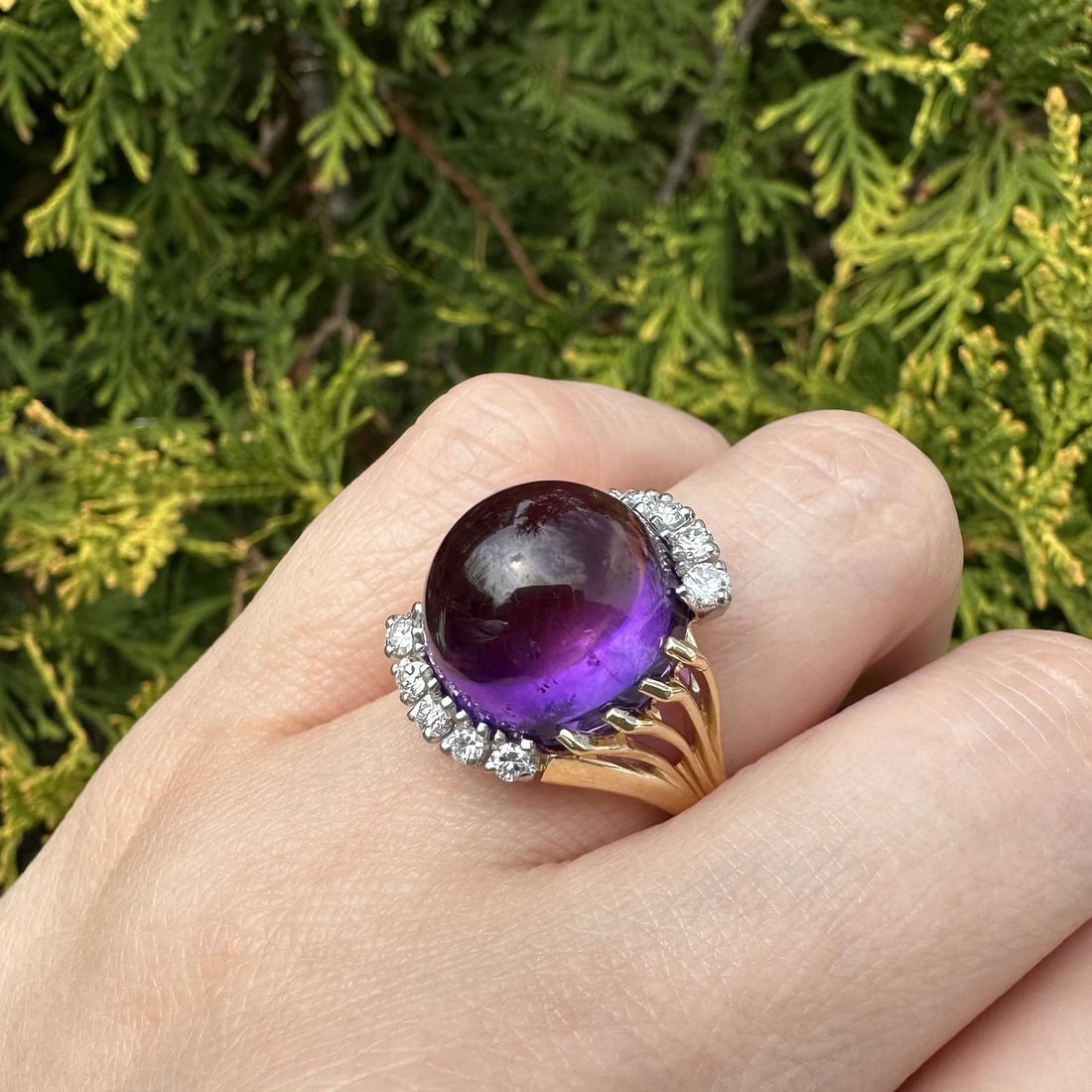 Cocktail Ring in 18k Yellow Gold with Cabochon Amethyst and Diamond Details: Cocktail Ring in 18k Yellow Gold with Cabochon Amethyst and Diamond Details This cocktail ring features a round cabochon-cut natural deep purple amethyst as the centerpiece, accented by ten round bril