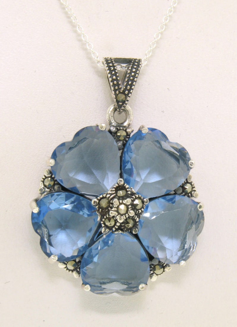 Floral Marcasite Sterling Silver Blue Topaz Heart Pendant with Chain: Floral Marcasite Sterling Silver Blue Topaz Heart Pendant with Chain This exquisite pendant showcases a stunning flower design crafted from solid .925 sterling silver. At the center, five heart-shaped