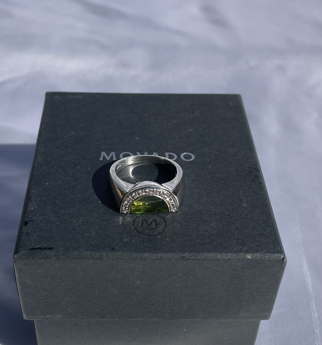 Movado 18K White Gold Peridot Diamond Ring with Box Size 6.75: Movado 18K White Gold Peridot Diamond Ring with Box Size 6.75 This exquisite Movado ring is crafted from 18K white gold and features a stunning peridot as its main stone, accompanied by approximately 