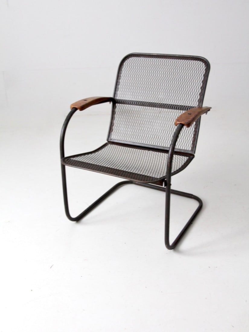 Vintage Mid-Century Black Metal Mesh Patio Chair with Wooden Arm Rests: Vintage Mid-Century Black Metal Mesh Patio Chair with Wooden Arm Rests This mid-century patio chair showcases a stylish black metal mesh design complemented by a unique 'bouncer' frame and wooden arm 