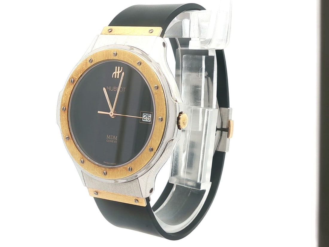Hublot MDM Ref. 1823.2 38mm wristwatch steel case gold tone bezel: Hublot MDM Ref. 1823.2 38mm wristwatch steel case gold tone bezel Pre-owned Hublot MDM wristwatch with a stainless steel case, black dial, black rubber strap, and gold tone bezel. This quartz analog w