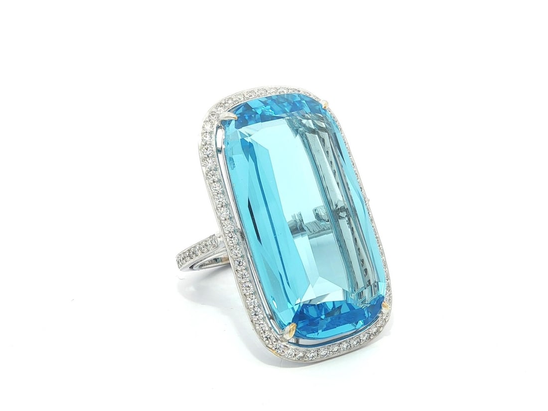 Handmade 18k White Gold 29.10ctw Cushion Blue Topaz Diamond Halo Ring: Handmade 18k White Gold 29.10ctw Cushion Blue Topaz Diamond Halo Ring This exquisite handmade ring features a stunning elongated cushion-cut natural blue topaz, weighing approximately 28 carats. The b