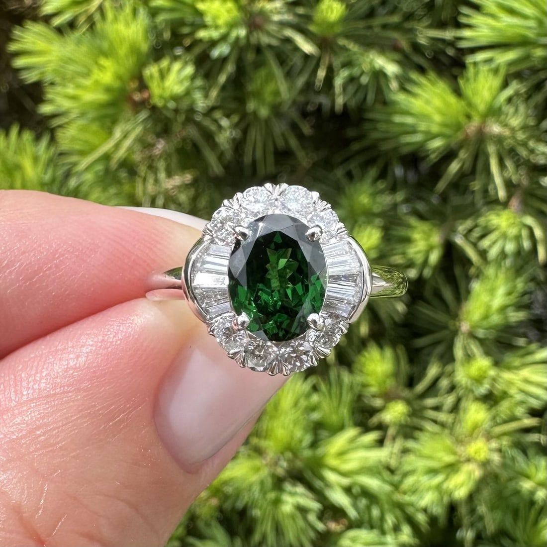 Platinum Flower Cocktail Ring with Oval Green Tsavorite and Diamond Halo: Platinum Flower Cocktail Ring with Oval Green Tsavorite and Diamond Halo This elegant platinum cocktail ring features a deep green natural oval-cut tsavorite weighing 1.48ct, set at the center and sur