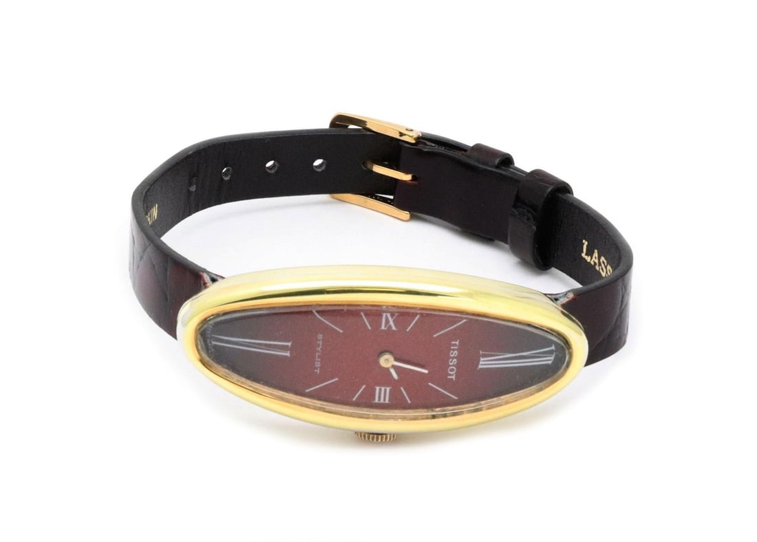 Ladies Hand Wound Tissot Stylist Oval Watch 18k Gold Case with Leather Strap: Ladies Hand Wound Tissot Stylist Oval Watch 18k Gold Case with Leather Strap This vintage Tissot Stylist ladies wristwatch features an 18k yellow gold long oval curved case with a red dial and large w