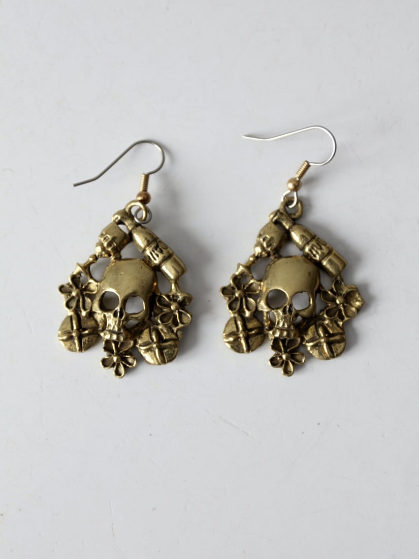 Mexican Gold Tone Skull Drop Earrings with Floral Motifs: Mexican Gold Tone Skull Drop Earrings with Floral Motifs These vintage skull dangle earrings feature a detailed gold tone finish with a central skull surrounded by floral and shield motifs. Marked Mex