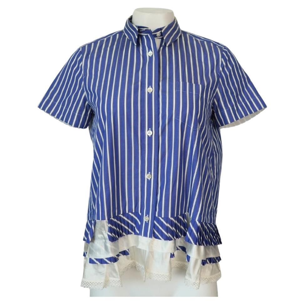 Sacai striped collared shirt blue white with pleated lace hem: Sacai striped collared shirt blue white with pleated lace hem Blue and white striped collared button-up shirt by Sacai, featuring pleats and lace details at the bottom. Made in Japan, this piece is ma