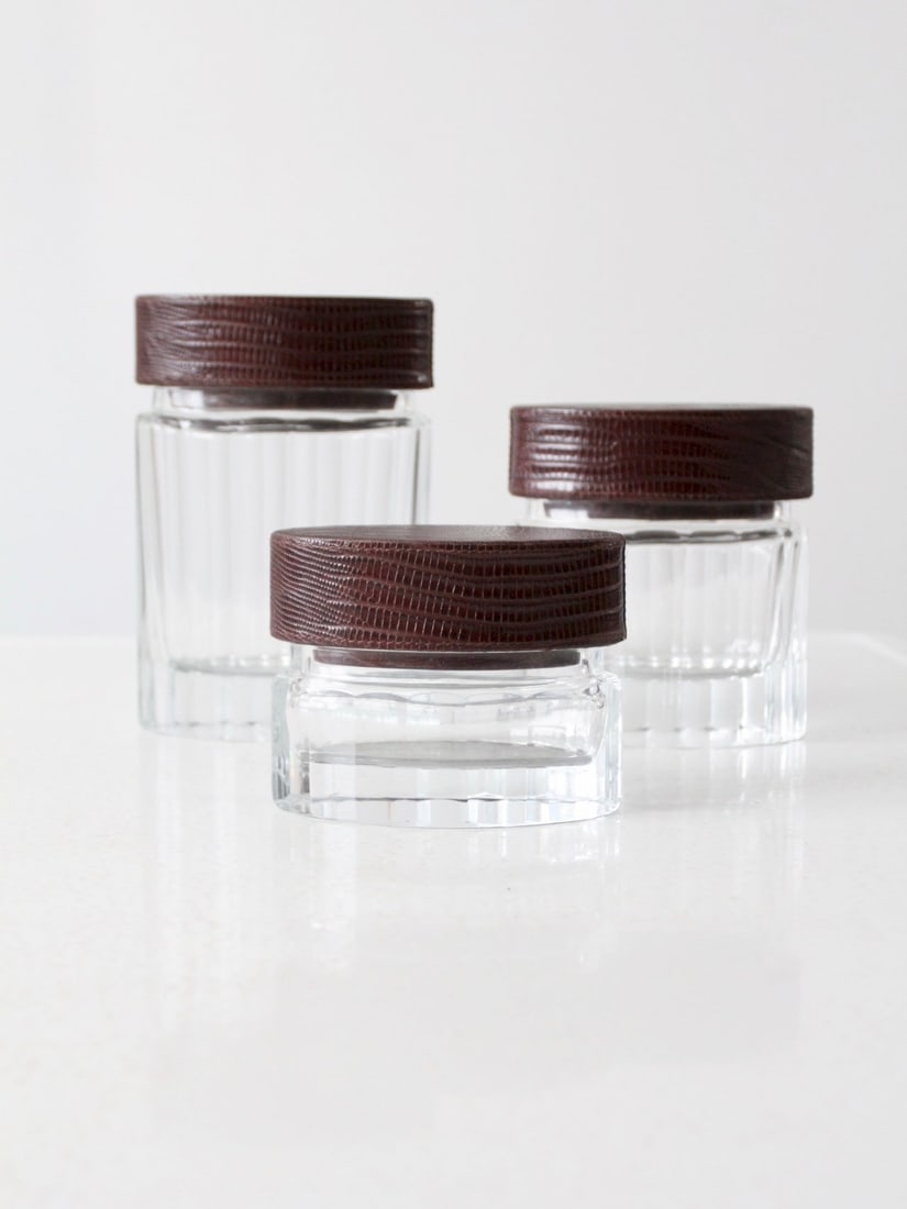Set of 3 Vintage Glass Jars with Leather Lids: Set of 3 Vintage Glass Jars with Leather Lids Enhance your home decor with this charming set of three vintage cut glass jars featuring elegant leather lids. Each jar showcases a unique graduated size 