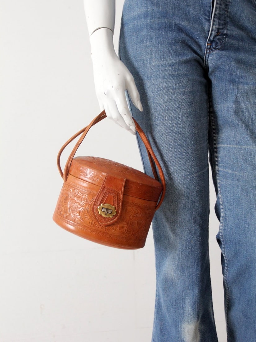 1950s Pillbox Tooled Leather Handbag with Brass Turnkey and Mirror: 1950s Pillbox Tooled Leather Handbag with Brass Turnkey and Mirror This early 1950s vintage handbag features a classic pillbox silhouette crafted from detailed tooled leather. It is accented by a bras