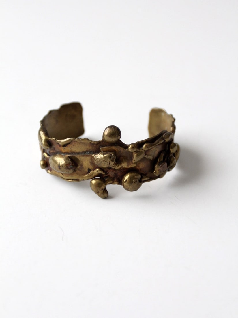 Vintage 1960s Brutalist Brass Cuff with Unique Patina: Vintage 1960s Brutalist Brass Cuff with Unique Patina This vintage 60s Brutalist cuff is expertly crafted from solid brass, showcasing a softly sculpted, dimensional texture that enhances its artistic