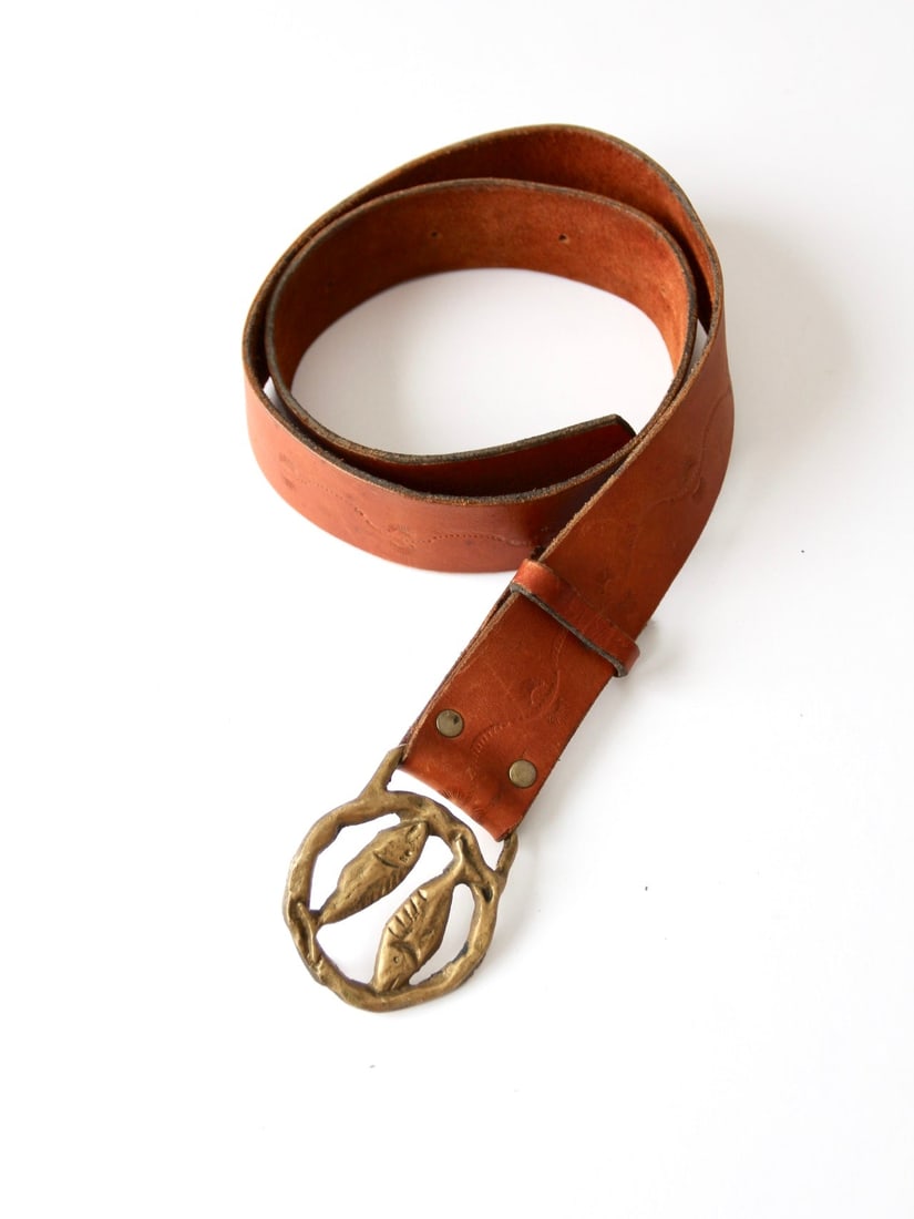 Vintage 70s Tooled Leather Belt with Pisces Zodiac Brass Buckle: Vintage 70s Tooled Leather Belt with Pisces Zodiac Brass Buckle Embrace the spirit of the 70s with this vintage hippie belt, featuring a beautifully tooled caramel leather strap and a striking Pisces 