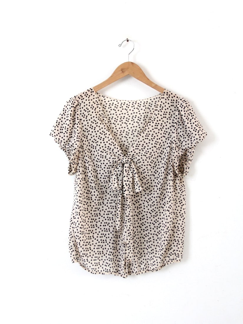 Charming Vintage Crepe Blouse with Dotted Heart Print: Charming Vintage Crepe Blouse with Dotted Heart Print This vintage crepe blouse showcases a delightful dotted heart print, enhancing its light and airy feel. The cream-colored fabric is embellished wi