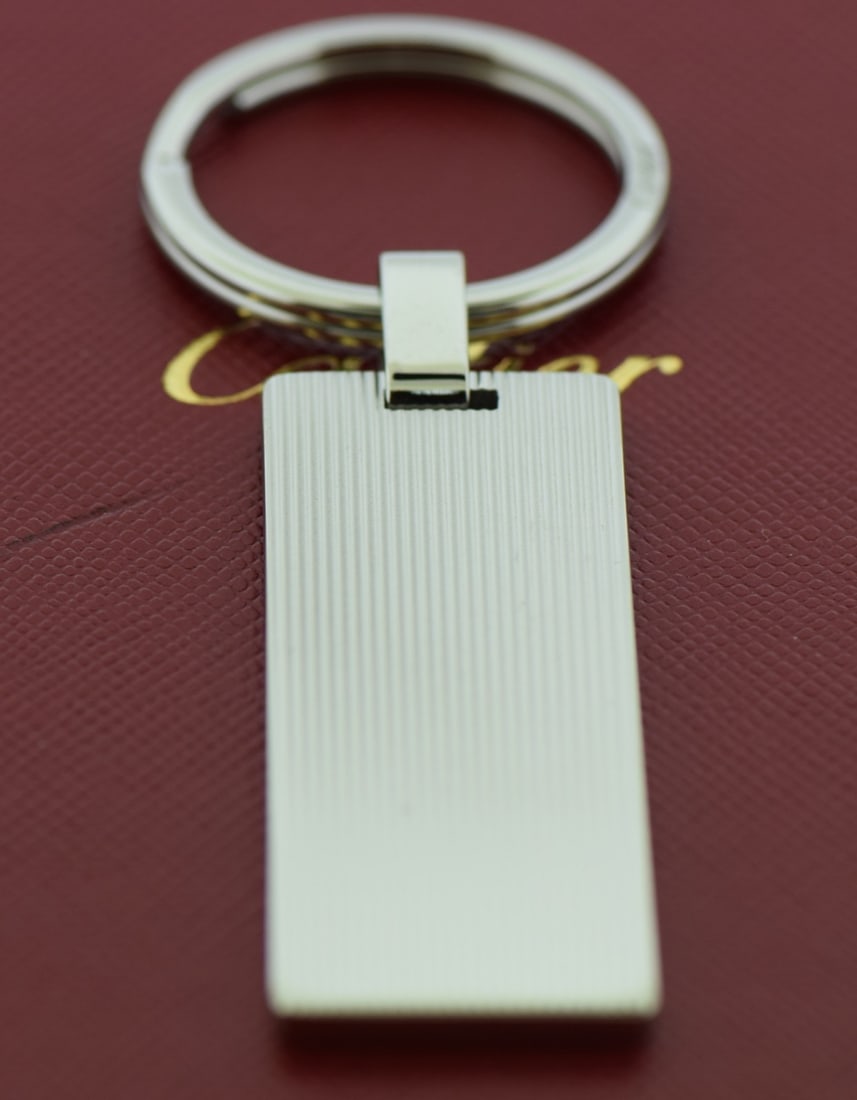 Unisex Silver Stainless Steel Key Ring by Cartier with Box: Unisex Silver Stainless Steel Key Ring by Cartier with Box This pre-owned Cartier key ring is crafted from stainless steel and features a sleek silver tone. Designed for unisex use, it offers a stylis