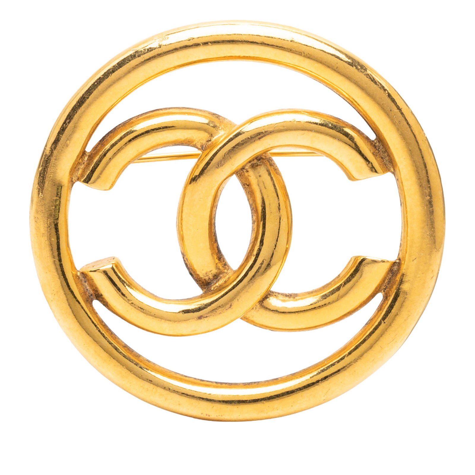 Chanel CC round brooch in gold plated metal: Chanel CC round brooch in gold plated metal Round Chanel CC brooch in gold-tone metal with a back pin closure. This costume jewelry piece is made in France. Condition is B+ with discoloration and scra
