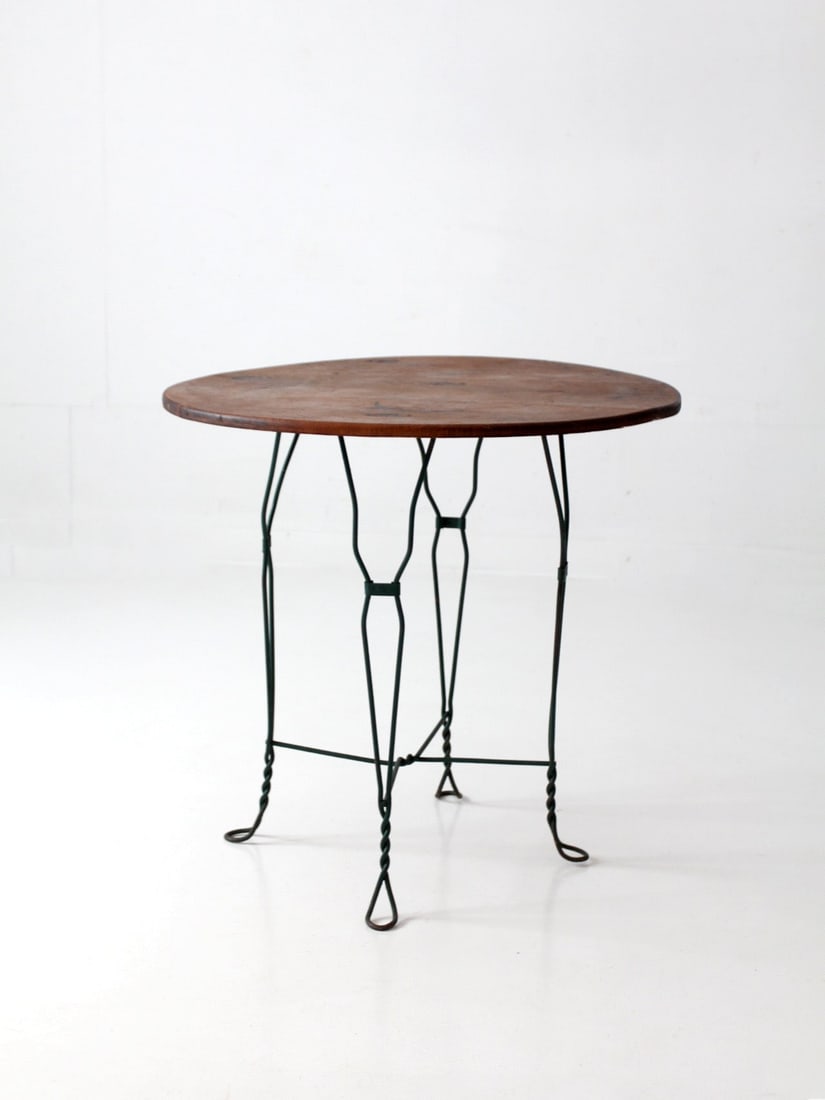 Round Wood Top Bistro Table with Green Wrought Iron Base: Round Wood Top Bistro Table with Green Wrought Iron Base Vintage mid-century bistro table featuring a round wood top and a deep green wrought iron base. The base is designed with elongated diamond for