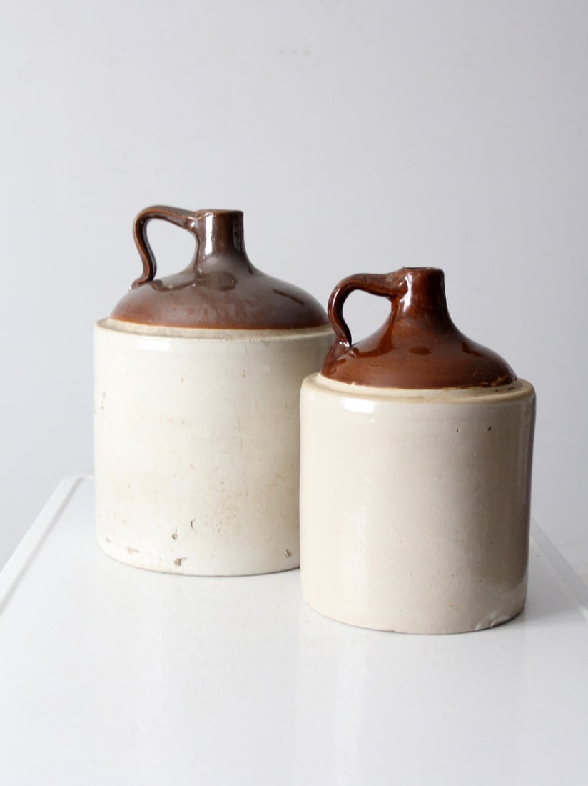Antique Stoneware Jugs Pair Rustic Farmhouse Decor: Antique Stoneware Jugs Pair Rustic Farmhouse Decor This pair of antique stoneware jugs showcases traditional utilitarian forms with beautifully aged surfaces and warm, earthy tones. One jug is distinc