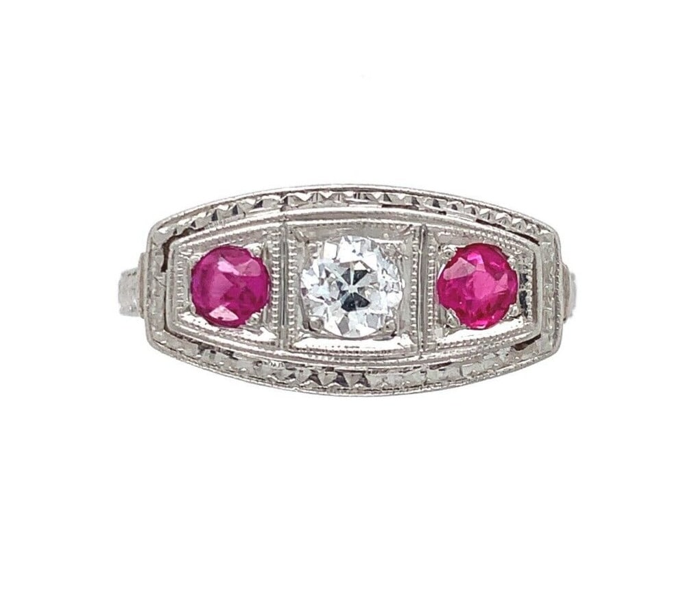 1920s Platinum Filigree Ring with .16ct Diamond and 2 Lab-Created Rubies: 1920s Platinum Filigree Ring with .16ct Diamond and 2 Lab-Created Rubies This stunning platinum ring features a beautifully crafted filigree design, showcasing a round diamond and two synthetic lab-cr