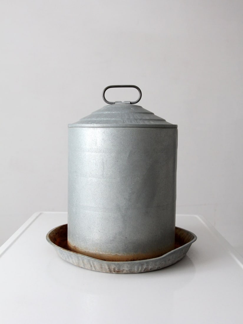 Galvanized Cylindrical Poultry Feeder with Lid and Tray Base: Galvanized Cylindrical Poultry Feeder with Lid and Tray Base This vintage galvanized chicken feeder features a classic cylindrical design with a fitted lid and a surrounding tray base. The feeder