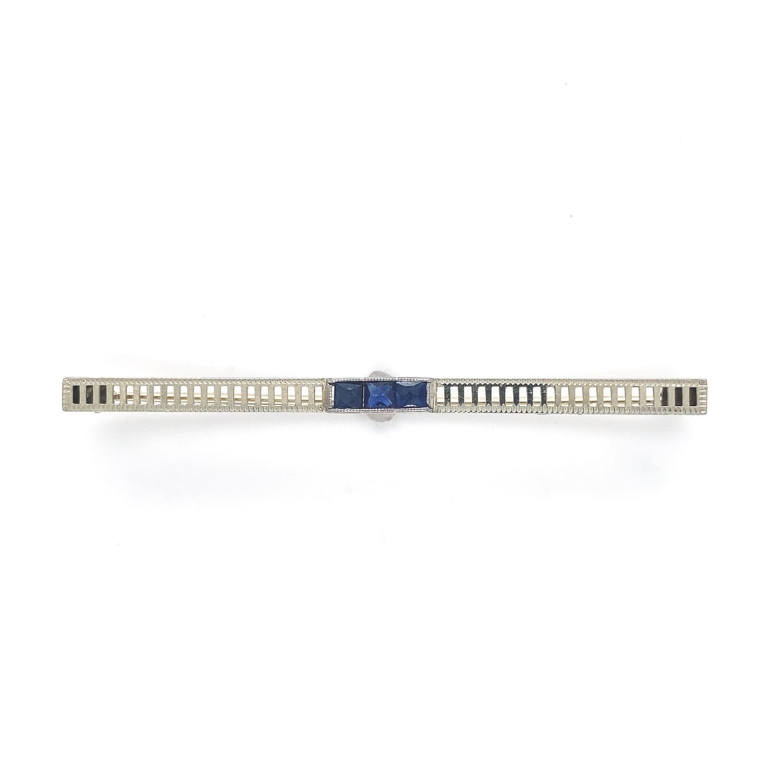 Art Deco pierced bar pin in 18k white gold with 3 lab created sapphires: Art Deco pierced bar pin in 18k white gold with 3 lab created sapphires Art Deco fine jewelry bar pin in 18k white gold, featuring three square synthetic lab-created blue sapphires. The piece is descr