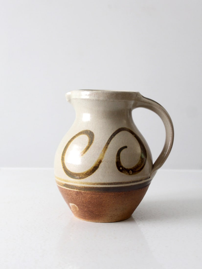 1996 Vintage Studio Pottery Pitcher with Golden Swirl Accents: 1996 Vintage Studio Pottery Pitcher with Golden Swirl Accents This vintage studio pottery pitcher, crafted in 1996, showcases a unique handmade design. The pitcher features a natural-toned glaze with 
