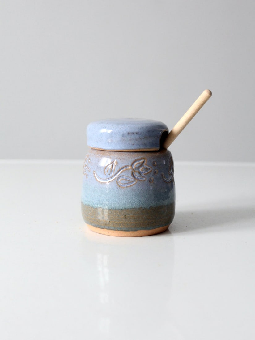 Studio Pottery Honey Jar with Wooden Dipper: Studio Pottery Honey Jar with Wooden Dipper This vintage studio pottery honey pot features a rounded shape and a soft blue glaze, complemented by an incised floral band around the body. It comes with 
