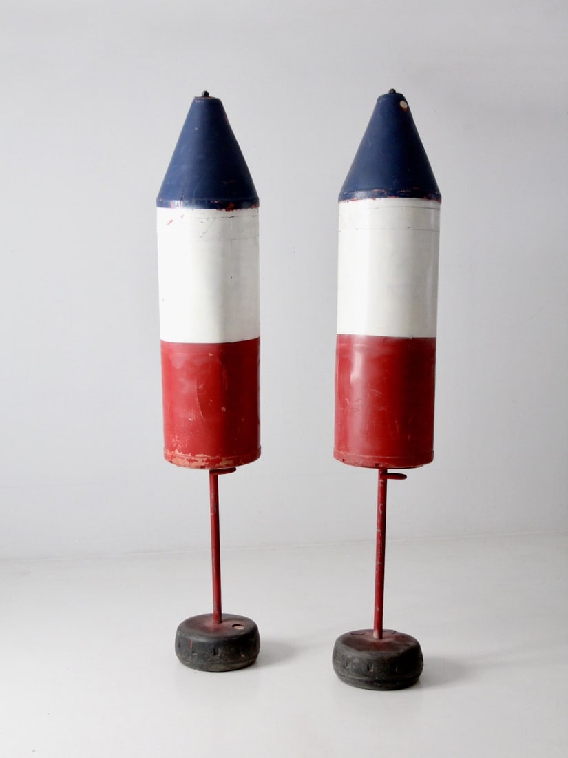 Pair of Vintage Maritime Marker Buoys 7 Feet Tall: Pair of Vintage Maritime Marker Buoys 7 Feet Tall Pair of vintage nautical marker buoys featuring elongated industrial forms, weighted cement bases, and worn red, white, and blue painted surfaces. The