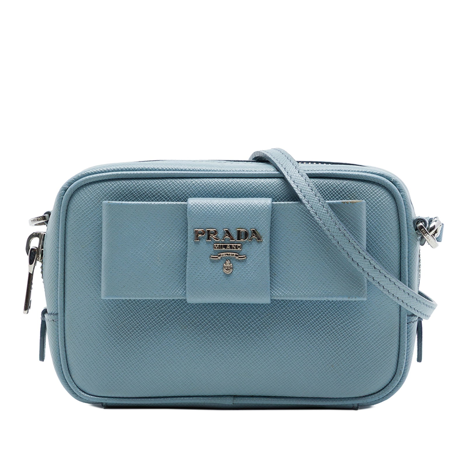 Prada Fiocco Bow Camera Crossbody Bag in Blue Saffiano Leather: Prada Fiocco Bow Camera Crossbody Bag in Blue Saffiano Leather Compact Prada camera bag crafted in blue Saffiano leather with a Fiocco bow detail. It features a detachable flat leather strap, top zip 