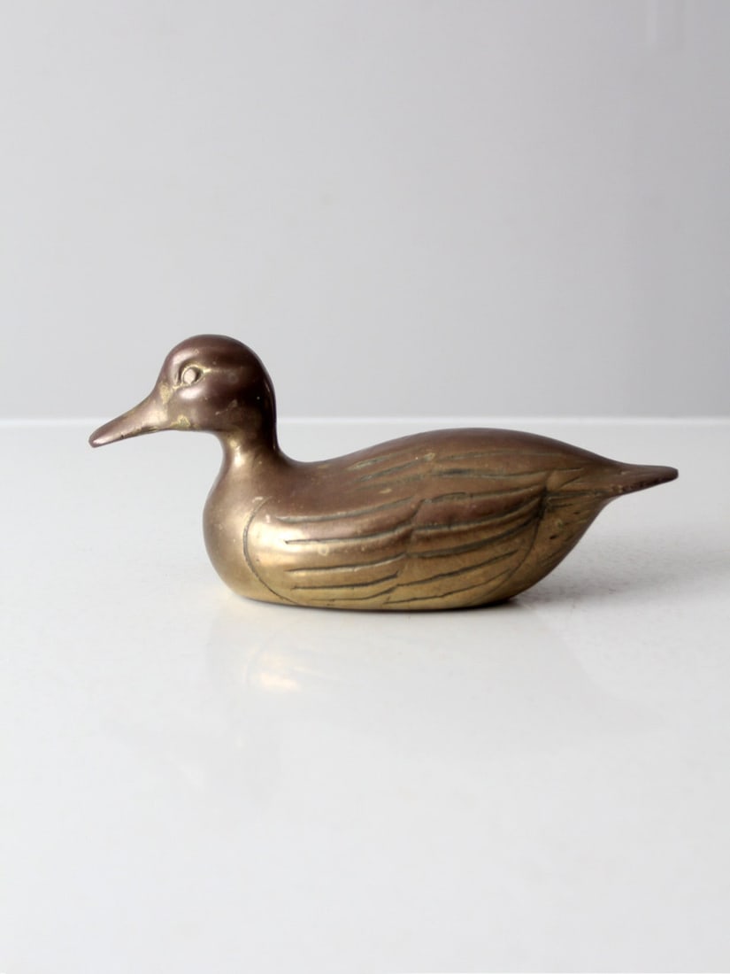Mid Century Brass Duck Figurine with Patina Finish: Mid Century Brass Duck Figurine with Patina Finish This mid 20th century brass duck figurine serves as a stunning accent piece for any decor. Its sleek lines and intricate detailing showcase an elegan