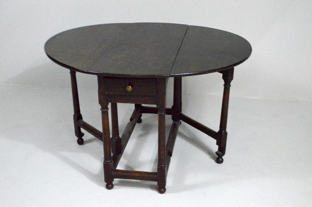 William and Mary Oak Gate-Leg Table, Circa 1860: With an oval drop leaf top supported by turned gate legs, over a central drawer, the whole raised on four turned legs with rectangular posts and ball feet supported by rectangular stretchers.
