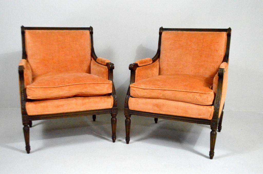 Pair of Louis XVI Style Walnut Bergeres: Each with moulded crest rail and stiles surrounding an upholstered back and seat cushion, the arms with upholstered arm pads and ending in carved scrolling stumps, the whole raised on four turned and 